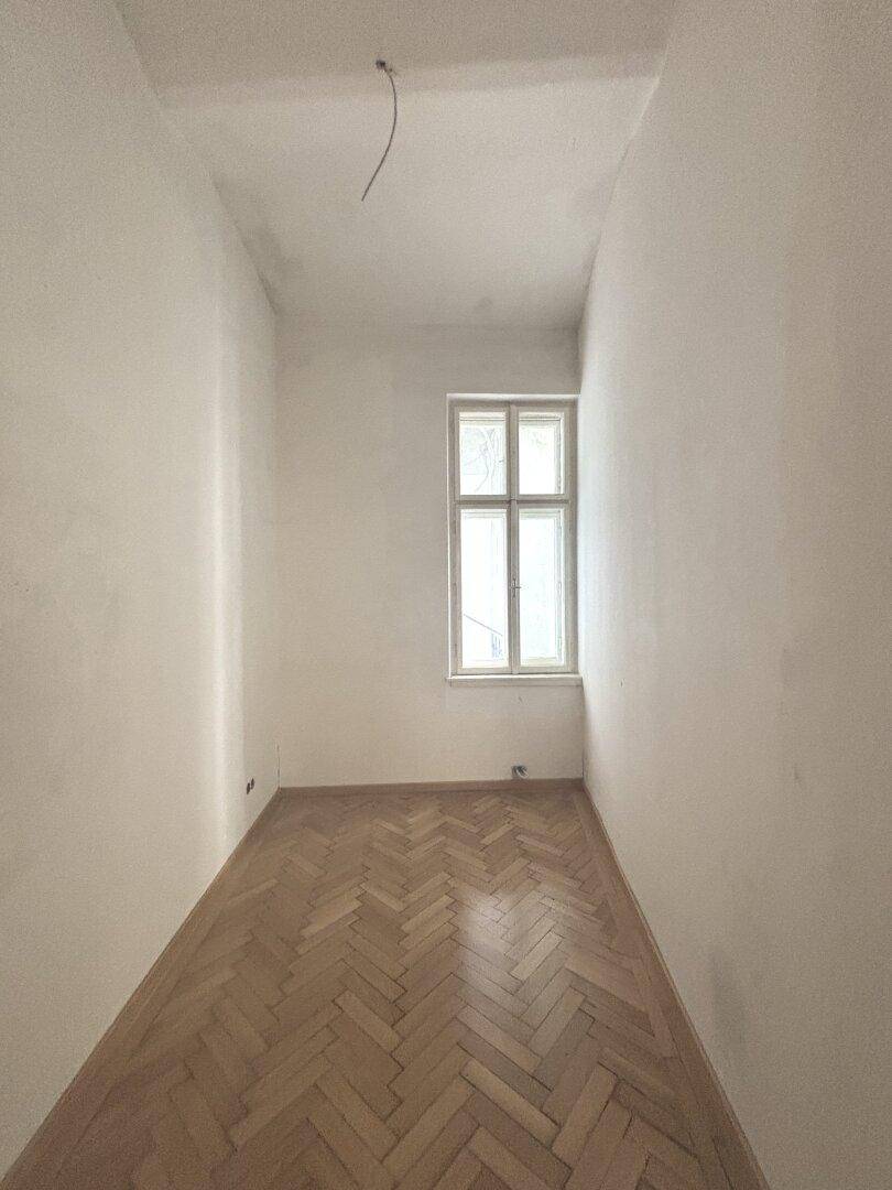 Kleineres Zimmer mit Fischgrätparkett und Fenster, ideal als Schlaf- oder Arbeitszimmer.