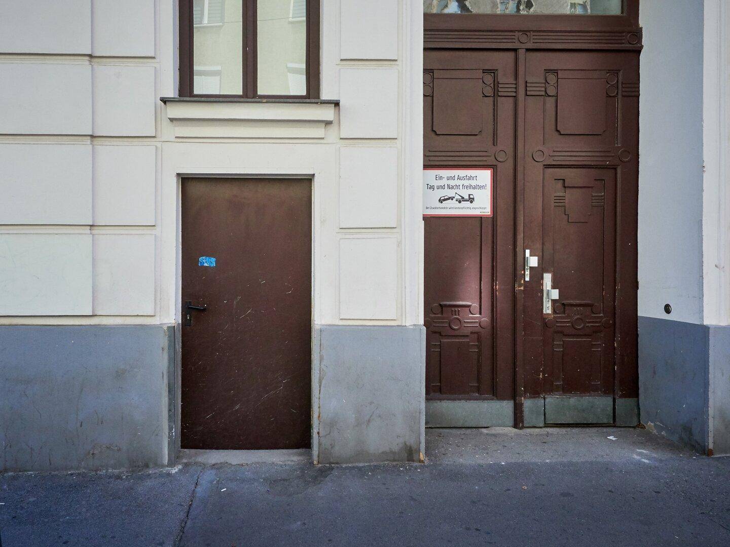 Zwei alte, braune Holztüren an einer hellen Gebäudefassade mit klassischer Architektur.