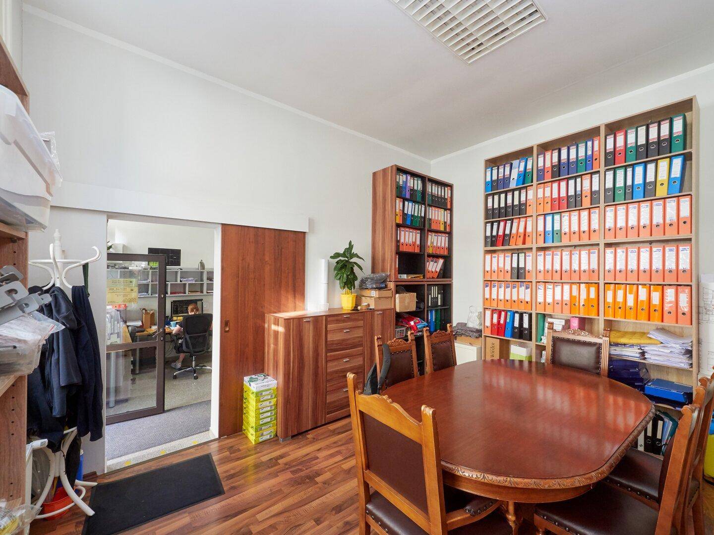 Geräumiges Büro mit großem Konferenztisch, Holzregalen voller Akten und Schiebetür zu weiterem Arbeitsbereich.