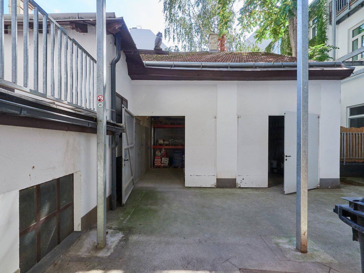 Hinterhof mit einem kleinen Gebäude und geöffneter Tür, die einen Blick in einen Lagerbereich ermöglicht.