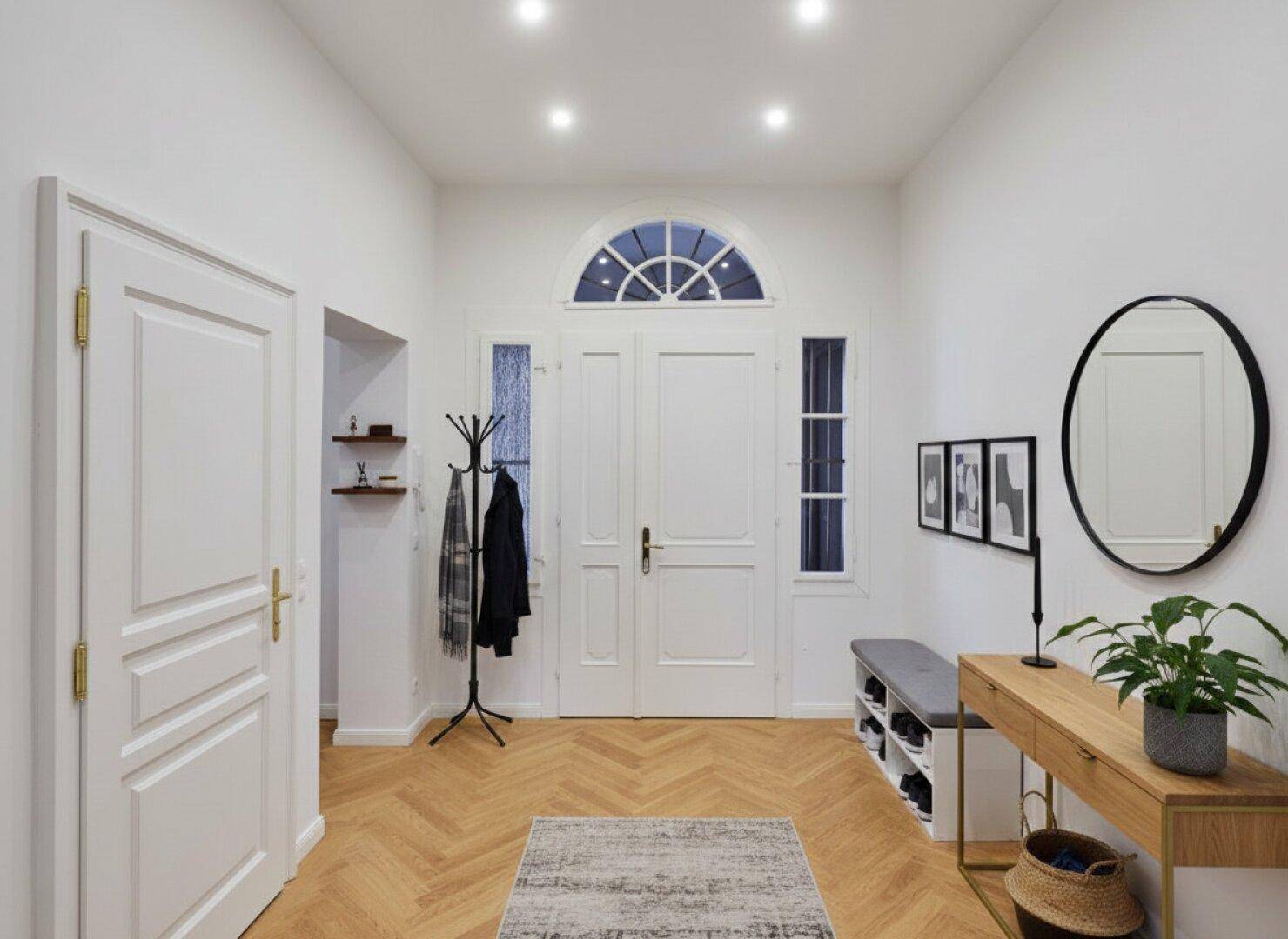 Heller Eingangsbereich mit Fischgrätparkett, Garderobe und dekorativem Spiegel.