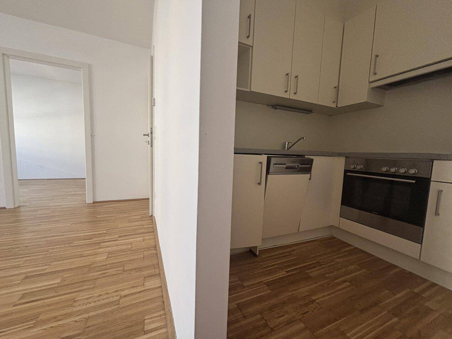 Blick vom Flur in die helle Küche mit Einbauschränken und Parkettboden.