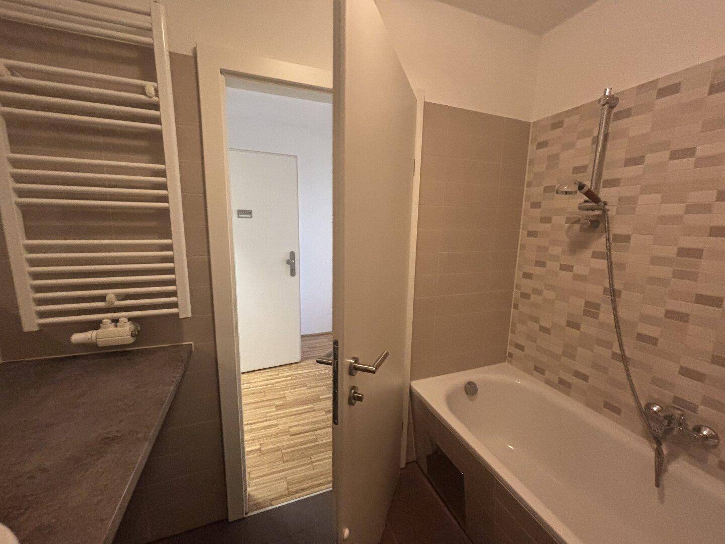 Badezimmer mit Badewanne, beheiztem Handtuchhalter und gemusterten Wandfliesen.