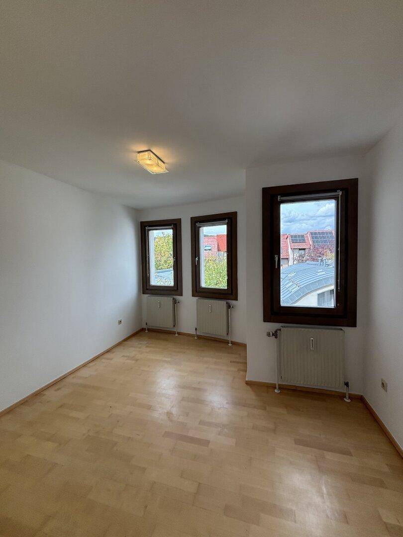 Geräumiges Schlafzimmer mit hellem Holzfußboden und mehreren Fenstern, die für gute Belichtung sorgen.