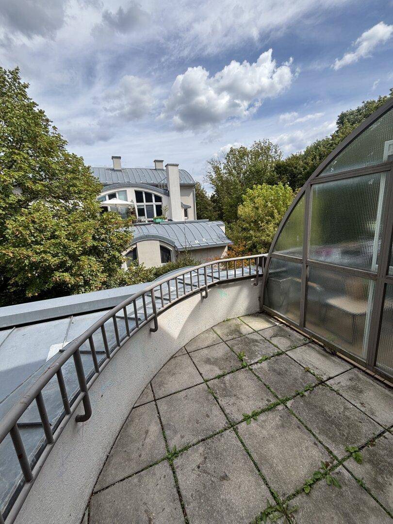 Terrasse mit Fliesenboden und Metallgeländer, umgeben von Bäumen und Blick auf die Nachbargebäude.