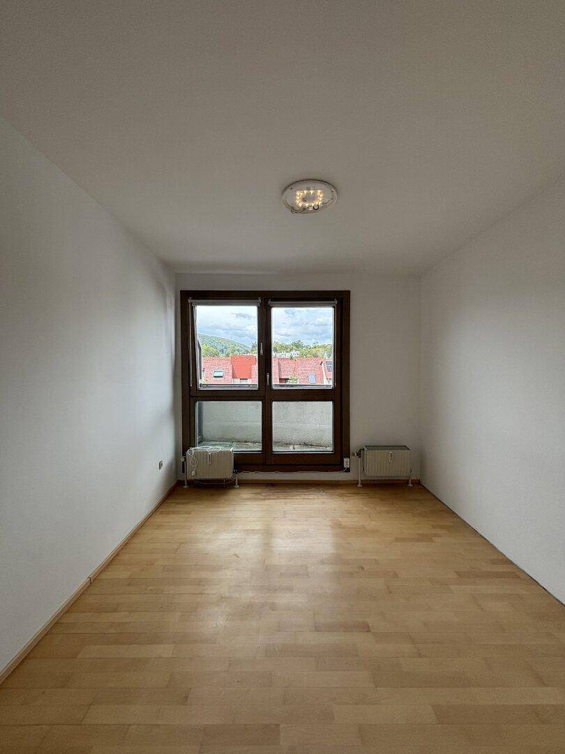 Helles Schlafzimmer mit Holzfußboden und einem großen Fenster, das viel Tageslicht in den Raum bringt.