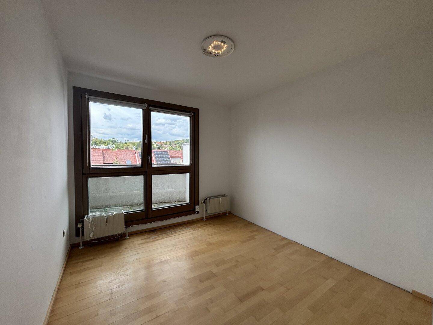 Geräumiges Schlafzimmer mit hellem Holzfußboden und einem großen Fenster, das den Raum gut belichtet.
