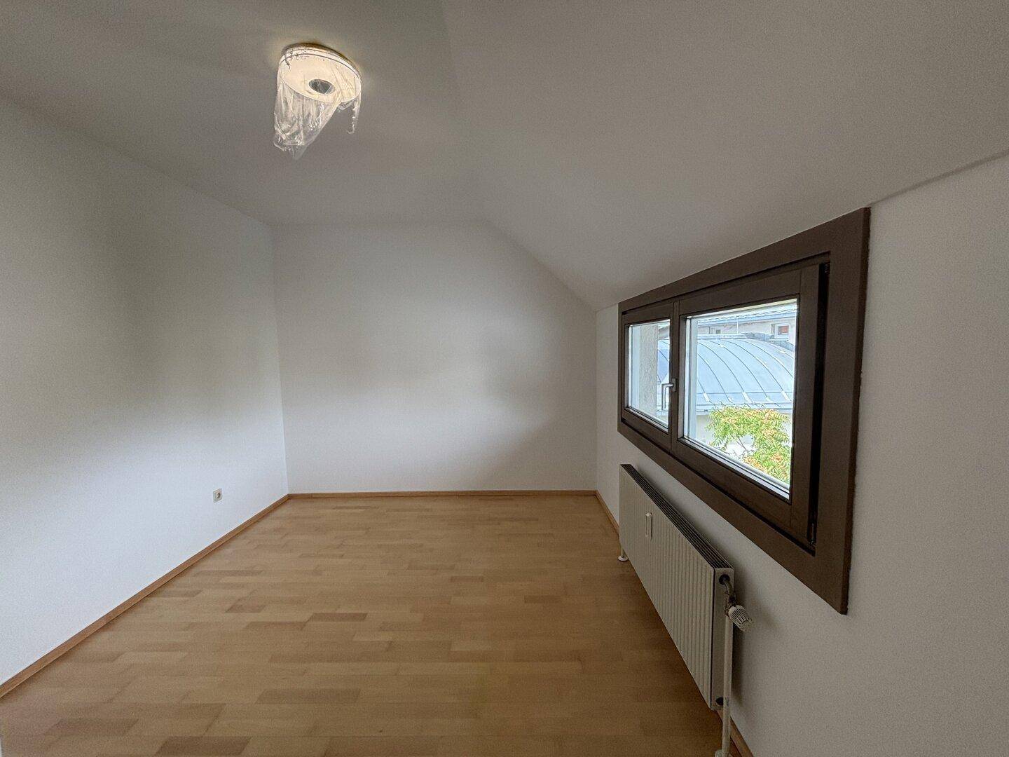 Helles Zimmer mit Holzfußboden, Dachschräge und zwei Fenstern, die den Raum mit Licht füllen.
