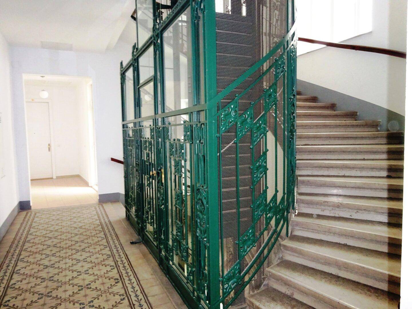 Historischer Flur mit kunstvollem Aufzug und Treppenhaus in einem eleganten Altbau.