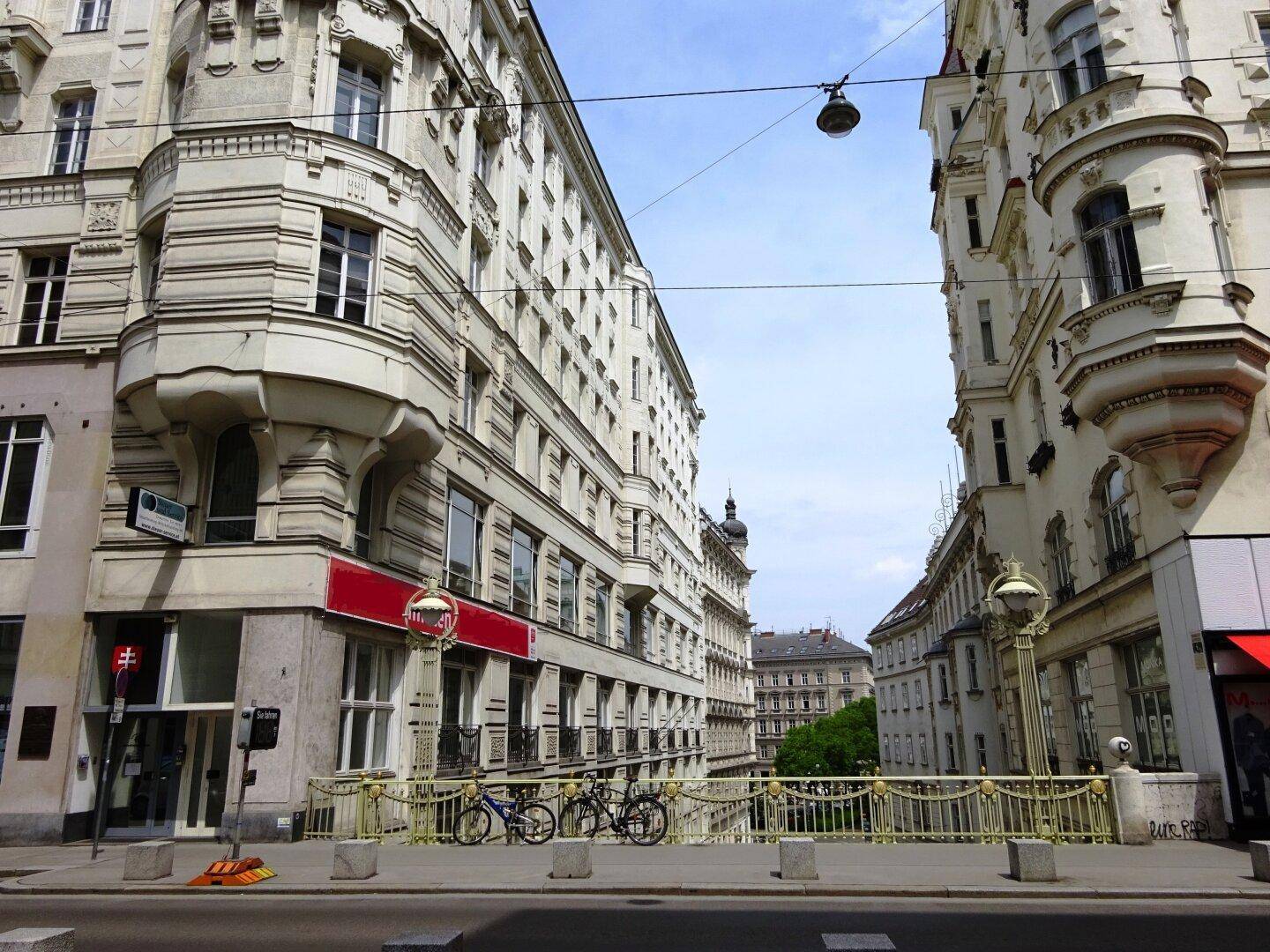Historische Straßenansicht mit eleganten Altbauten und einer Brücke unter blauem Himmel.