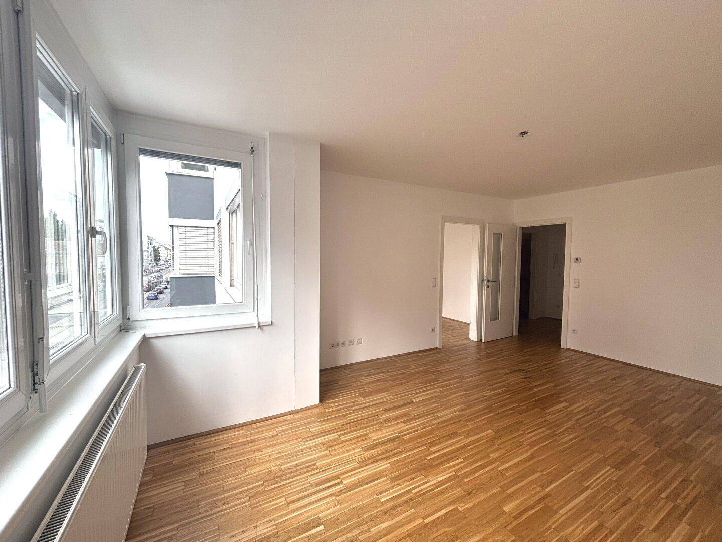 Helles, leeres Wohnzimmer mit großen Fenstern und Parkettboden, bietet viel Gestaltungspotenzial.