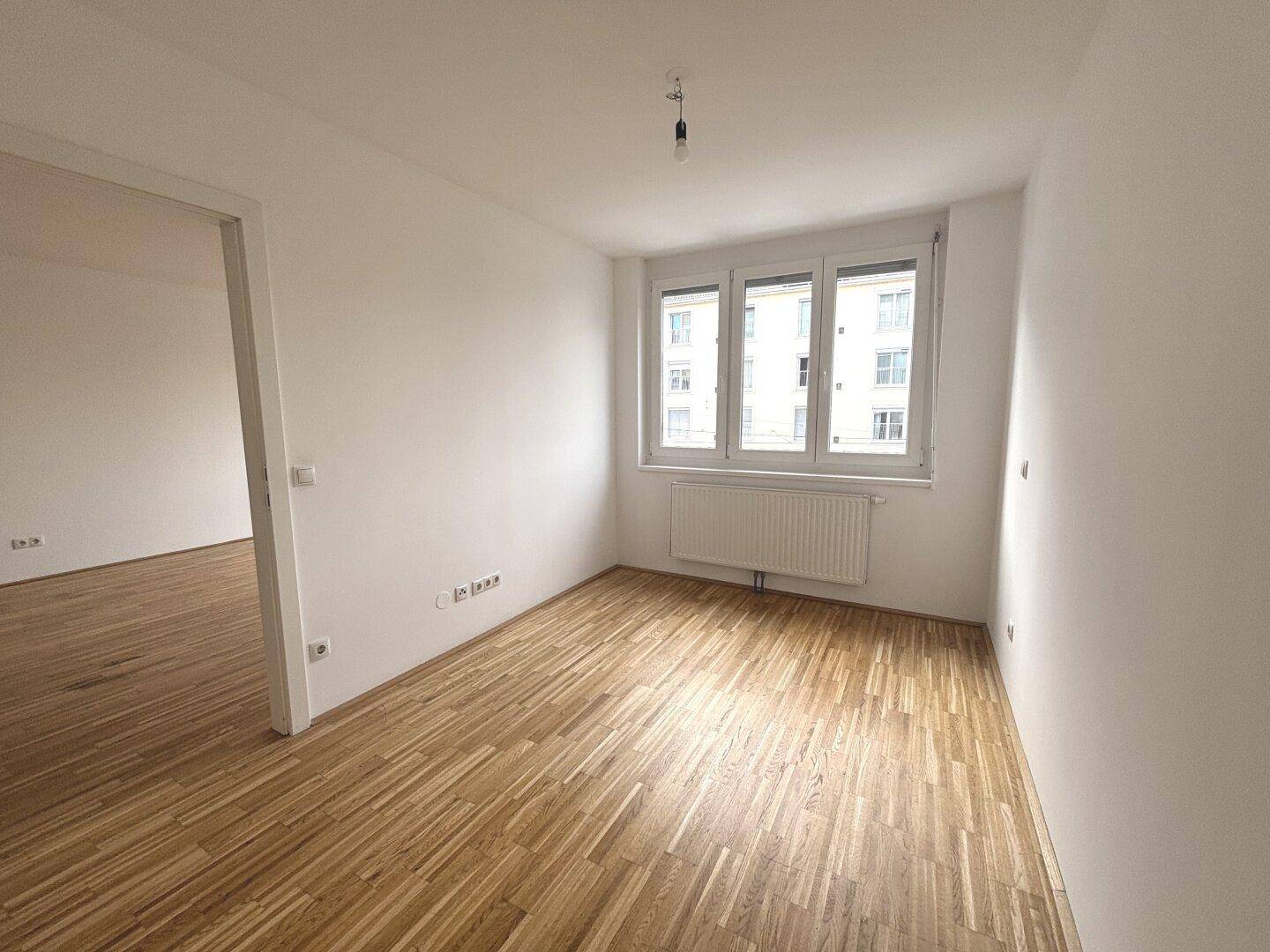 Leeres Schlafzimmer mit Parkettboden und Fensterfront, ideal für eine helle Einrichtung.