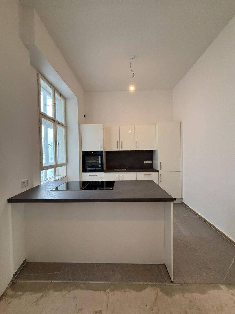 Moderne Küche mit weißen Hochglanzschränken, Kochinsel und großem Fenster.