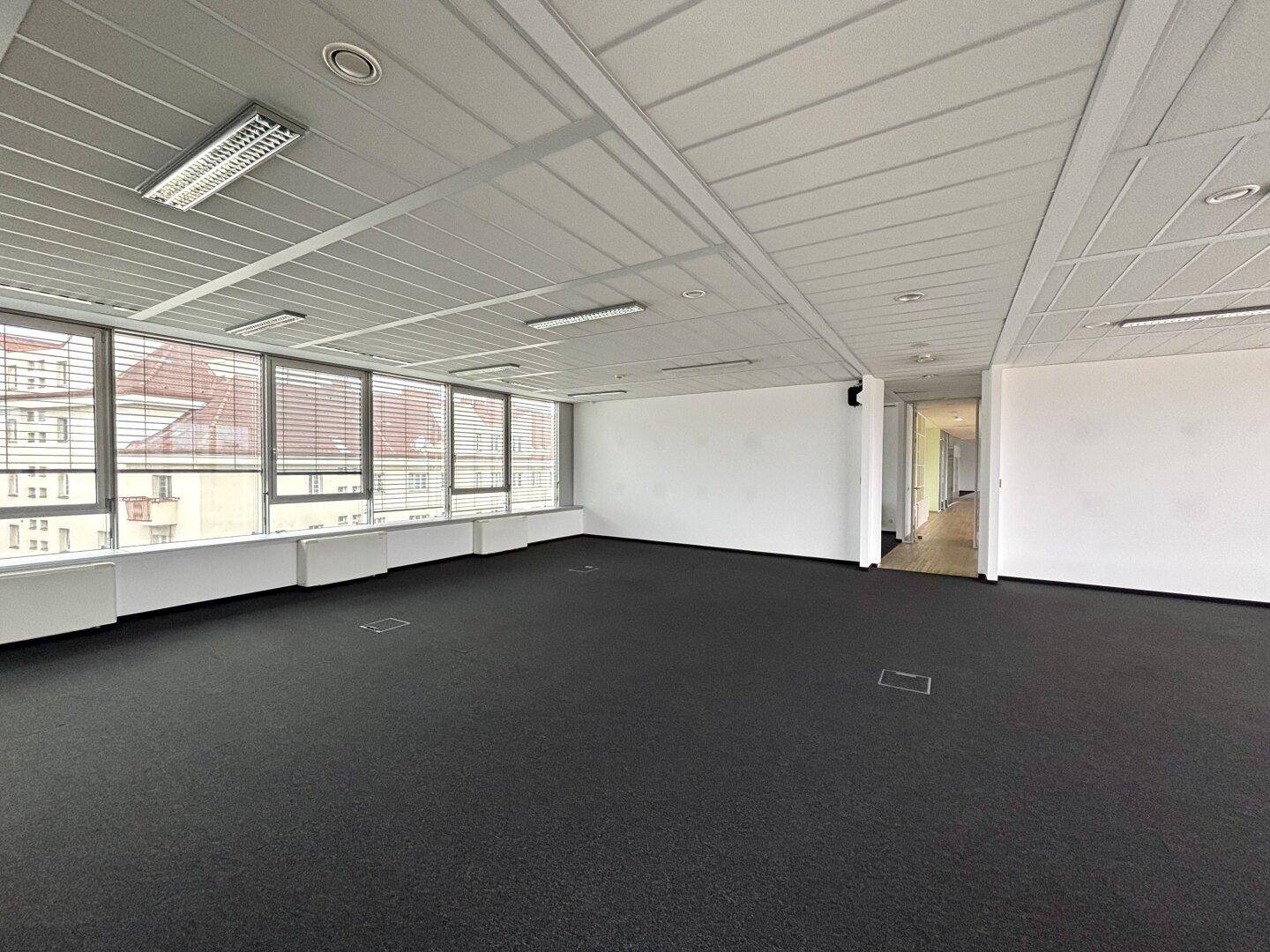 Offener Bürobereich mit Teppichboden, großen Fenstern und Blick auf die Umgebung.