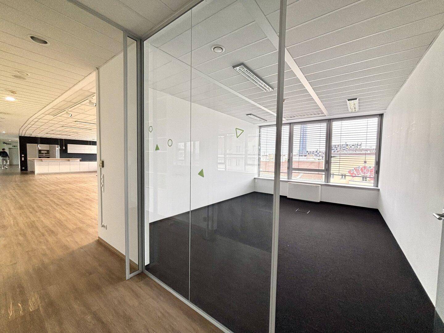 Büroraum mit Glastrennwand, Teppichboden und Blick auf die Stadt.