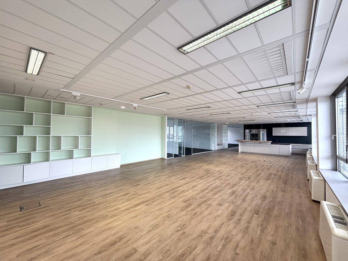Großzügiger Bürobereich mit Holzboden, integrierten Regalen und Blick auf eine Küchenzeile.