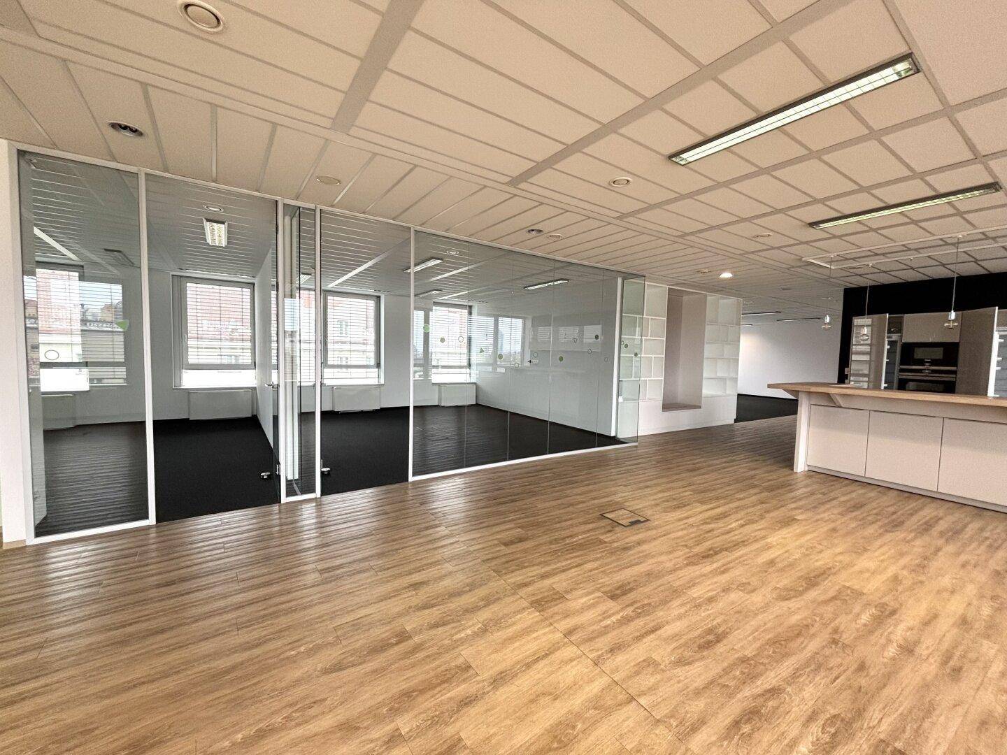 Offener Bürobereich mit Holzboden, Glaswänden und Blick in separate Arbeitszimmer.