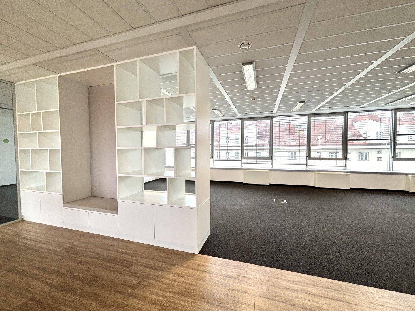 Bürobereich mit Holzboden und integriertem Regal, das als Raumteiler dient.
