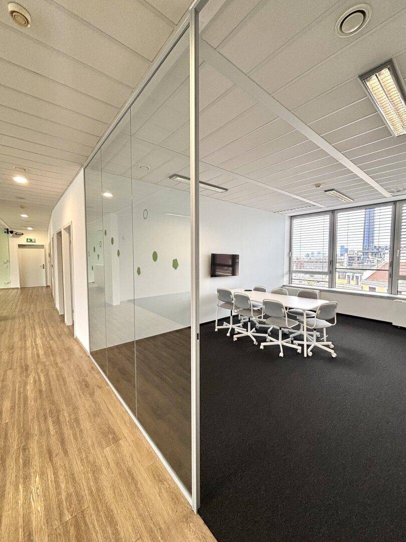 Moderner Konferenzraum mit Glastrennwand, Teppichboden und Blick auf den Flur.