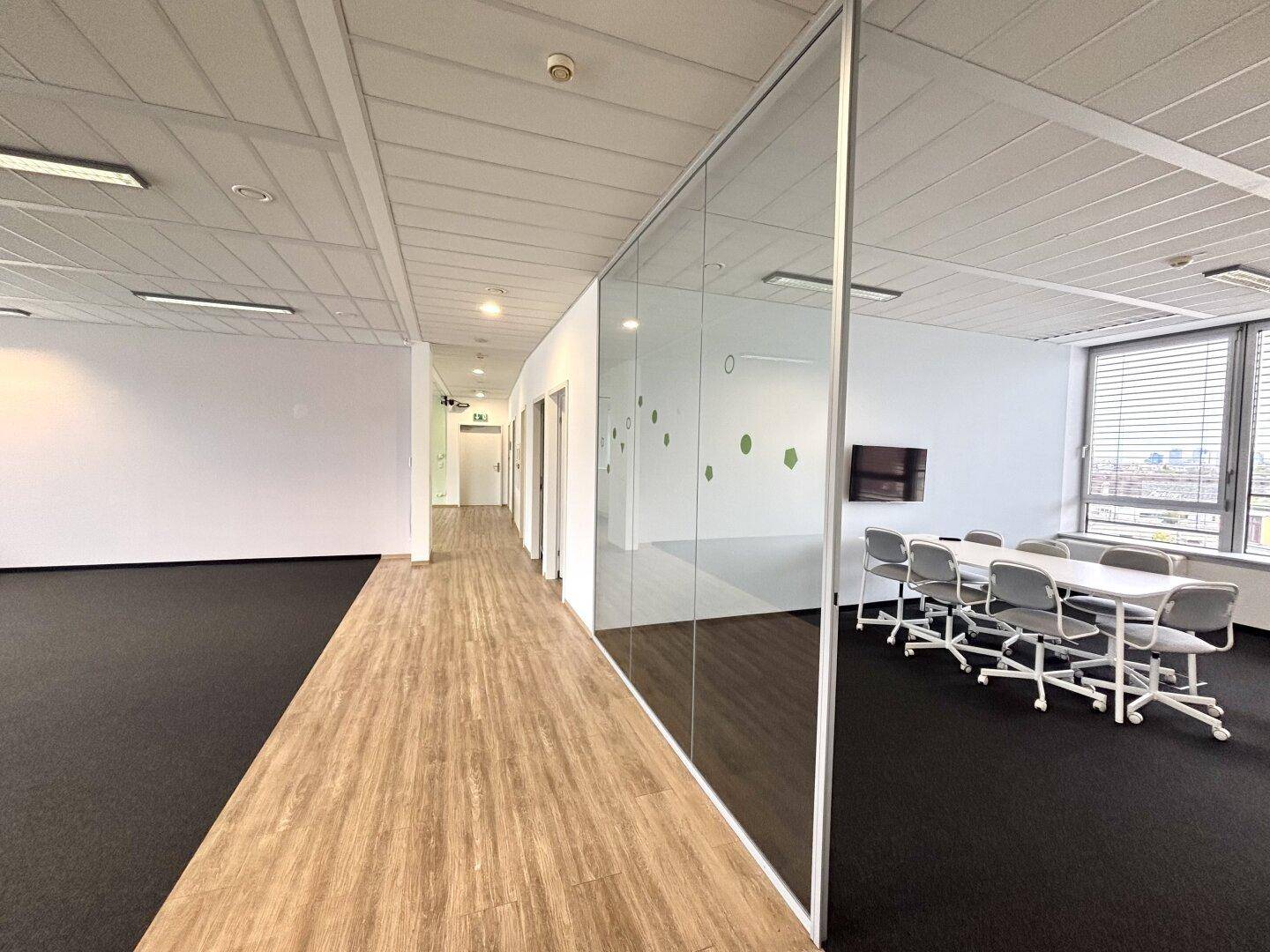 Heller Konferenzraum mit Glastrennwand, Teppichboden und Blick auf den Flur.