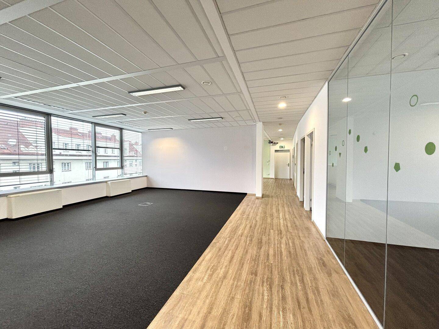 Langer Bürogang mit Holzboden, Teppichbereich und Blick auf die Fensterfront.