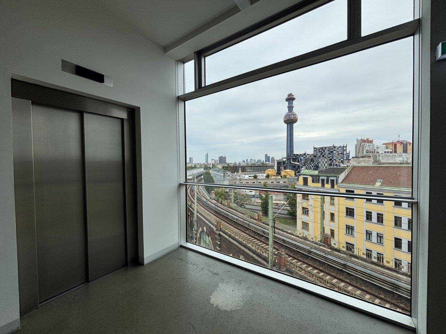Heller Aufzugsbereich mit Panoramablick auf die Stadt, Bahngleise und markante Gebäude.