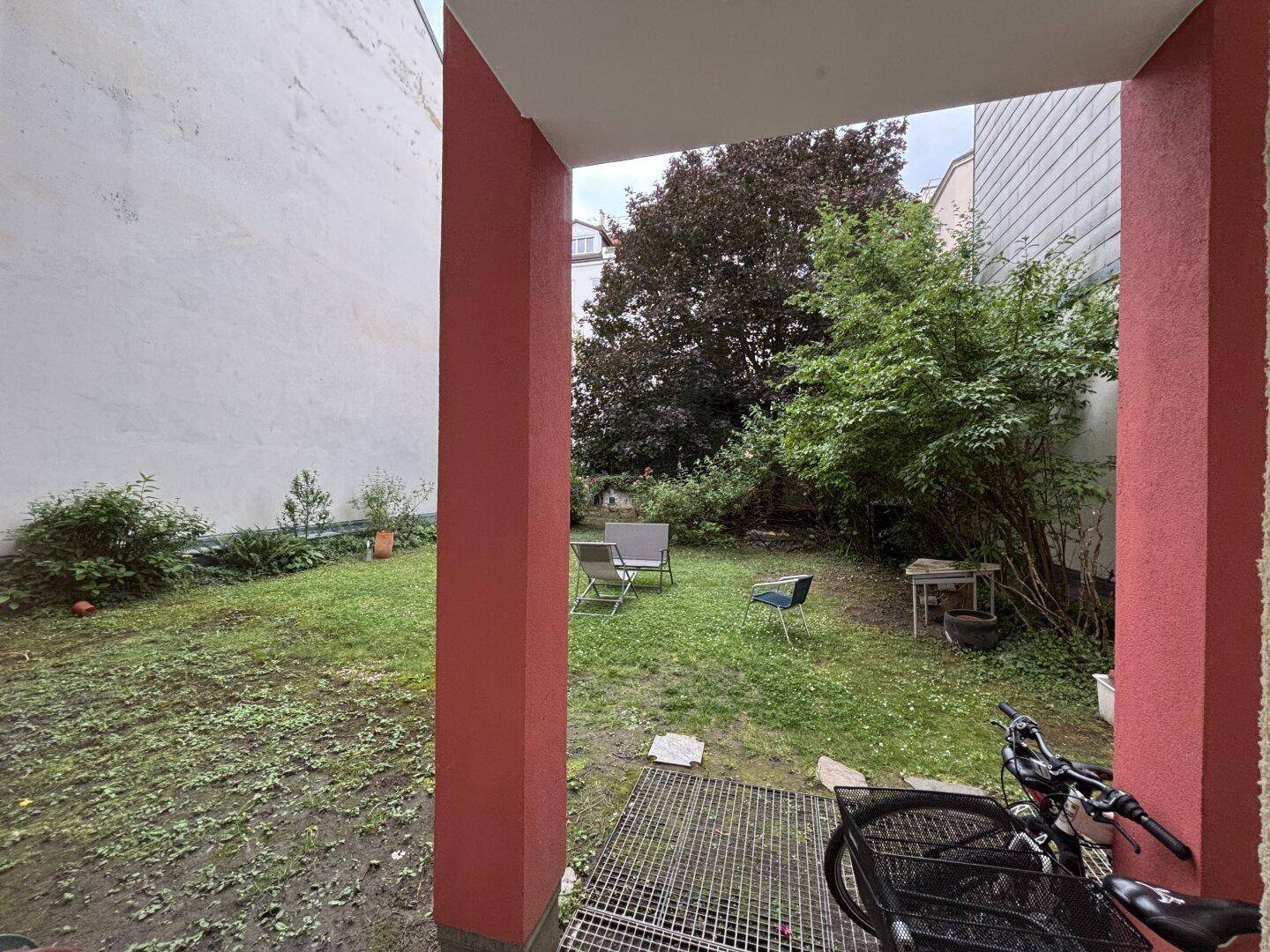 Blick auf einen grünen Gartenbereich von einem überdachten Außenbereich aus.