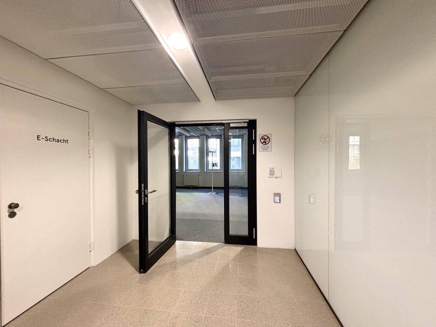 Heller Flur mit Glastür, die zu einem Büro führt, und schlichten weißen Wänden.