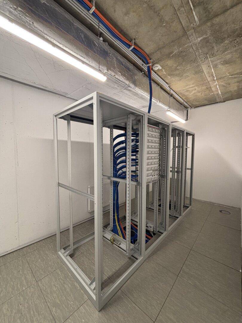 Technischer Raum mit Serverracks, sichtbaren Kabeln und industrieller Deckenkonstruktion.