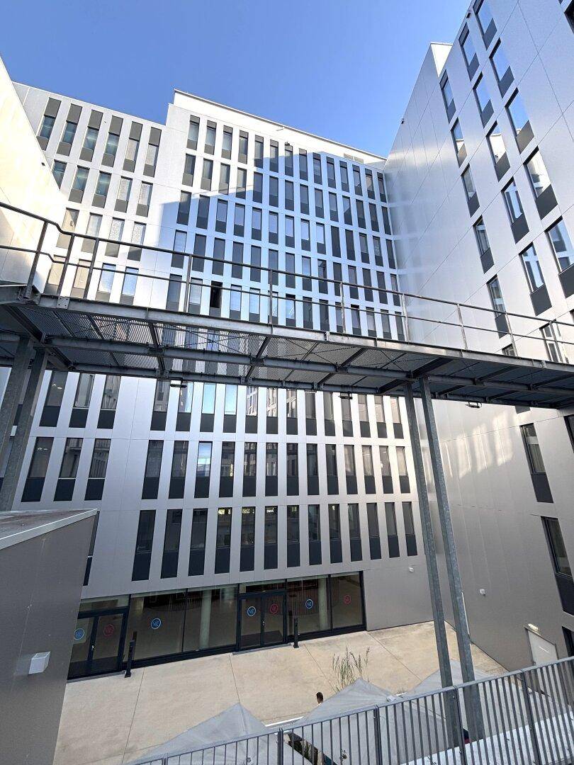 Moderne Gebäudefassade mit vielen Fenstern und einem erhöhten Übergang zwischen den Gebäudeteilen.