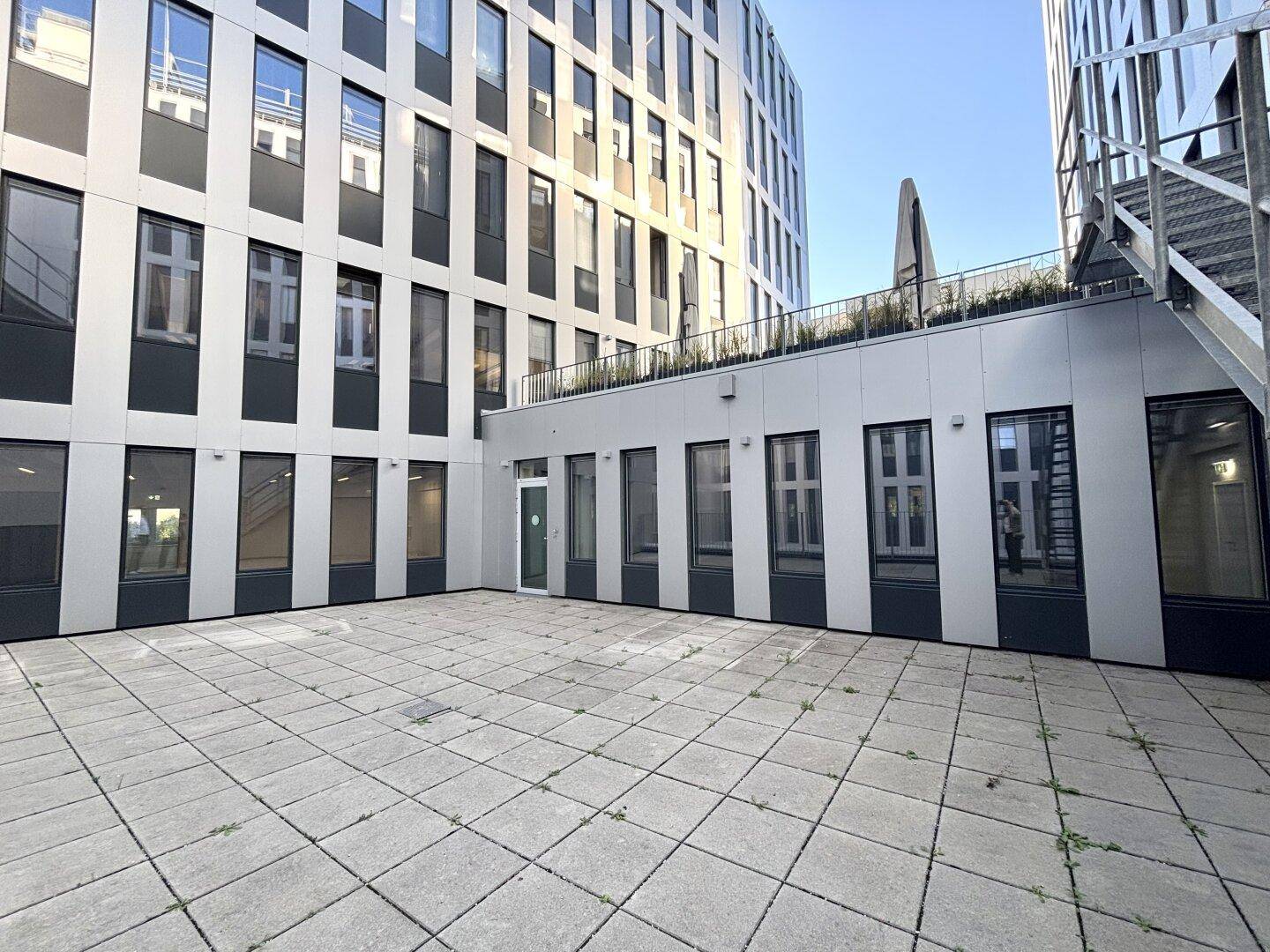 Großer, gepflasterter Innenhof zwischen modernen Gebäuden, ideal für zukünftige Gestaltung.