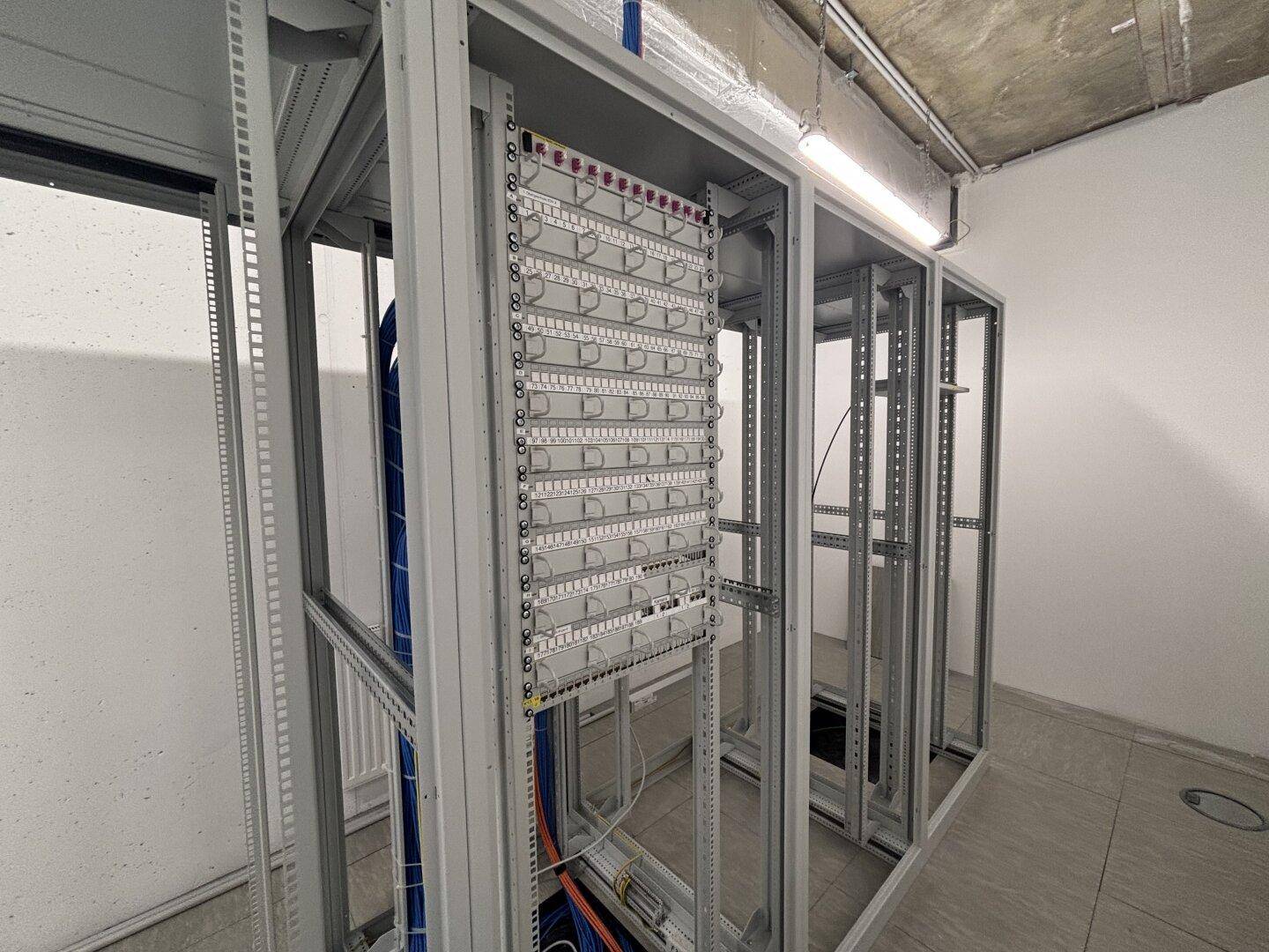 Technischer Raum mit offenen Serverschränken und sichtbaren Kabelinstallationen an der Decke.