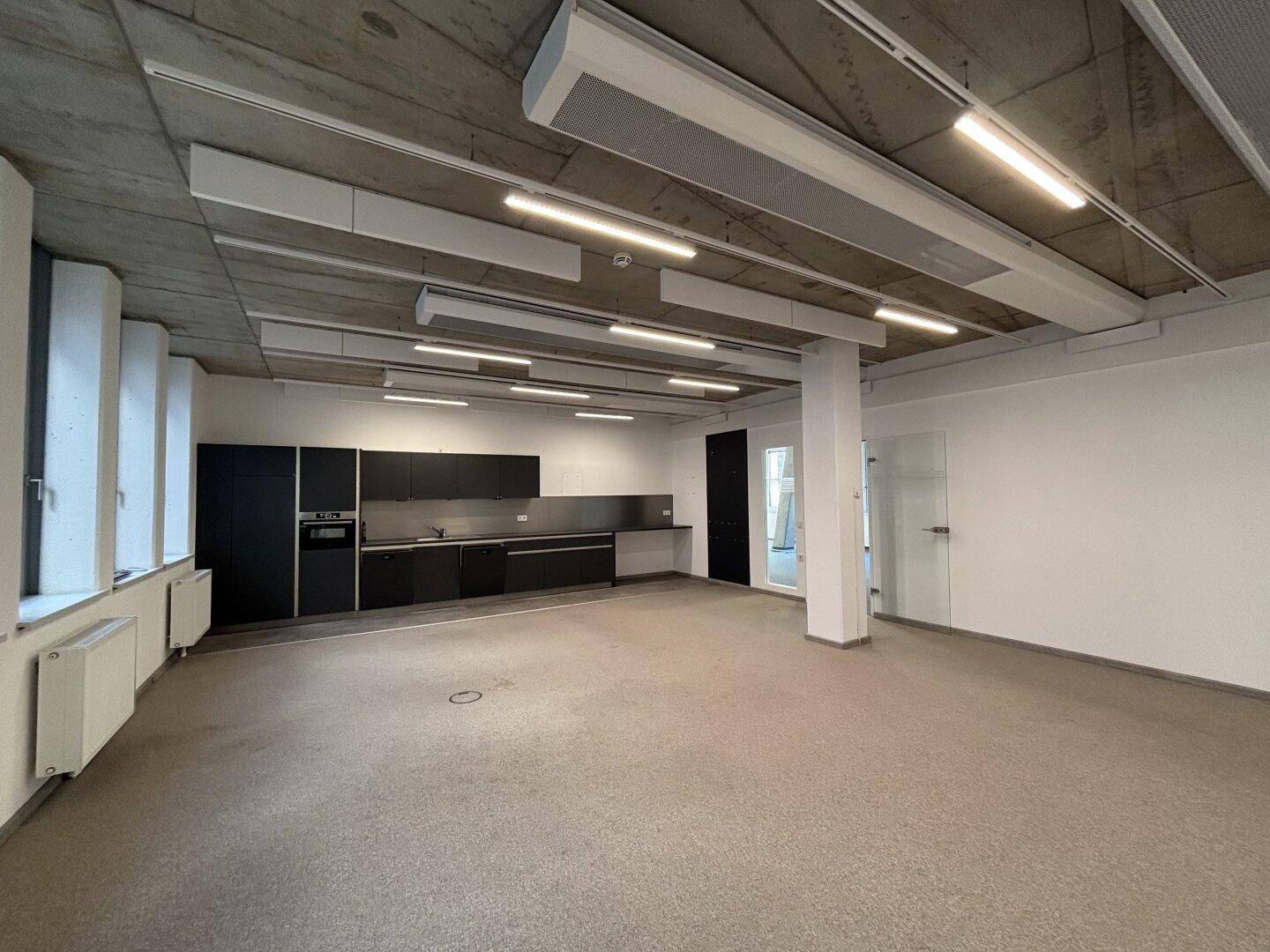 Geräumiger Küchenbereich im Büro mit dunkler Einbauküche, Säule und Glastür.