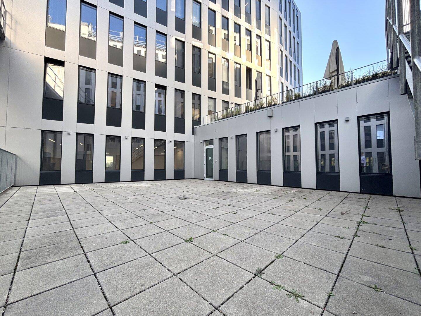 Weitläufiger, leerer Innenhof mit Pflastersteinen, umgeben von modernen Bürogebäuden.