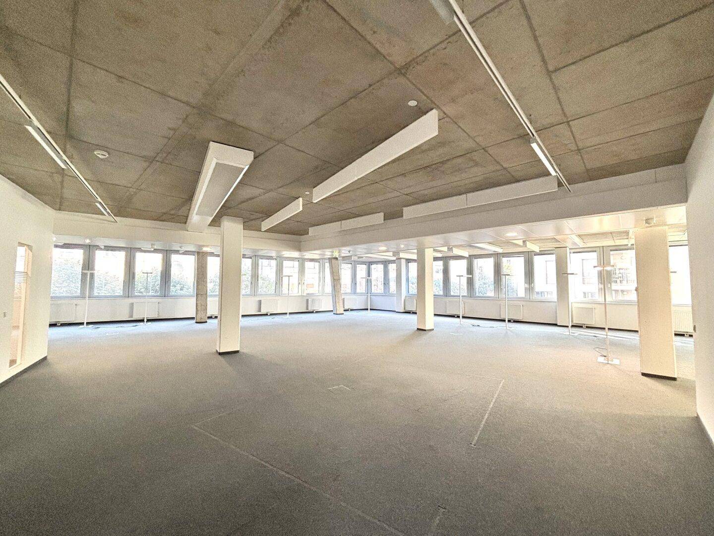 Großer, offener Bürobereich mit Säulen, vielen Fenstern und Teppichboden, bereit zur Gestaltung.