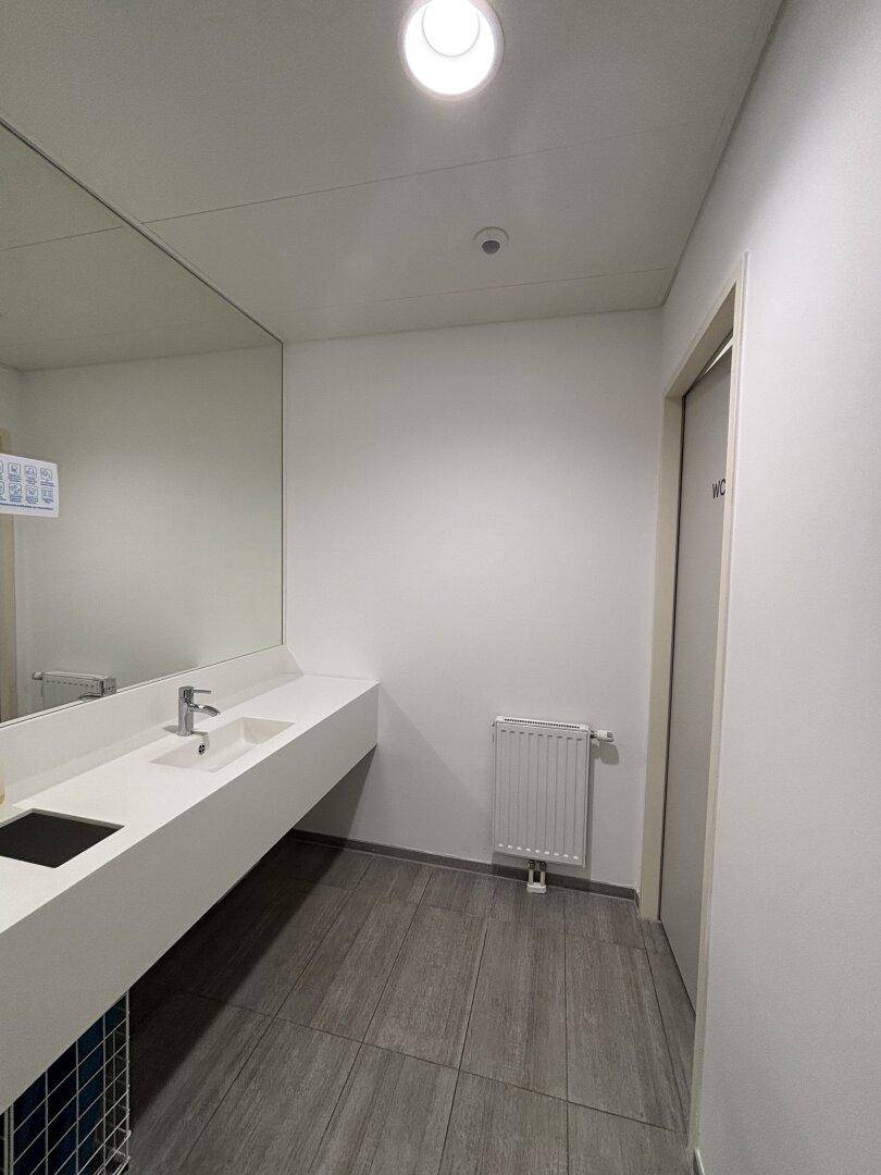 Moderner Waschraum mit großem Spiegel, weißem Waschtisch und Heizkörper an der Wand.