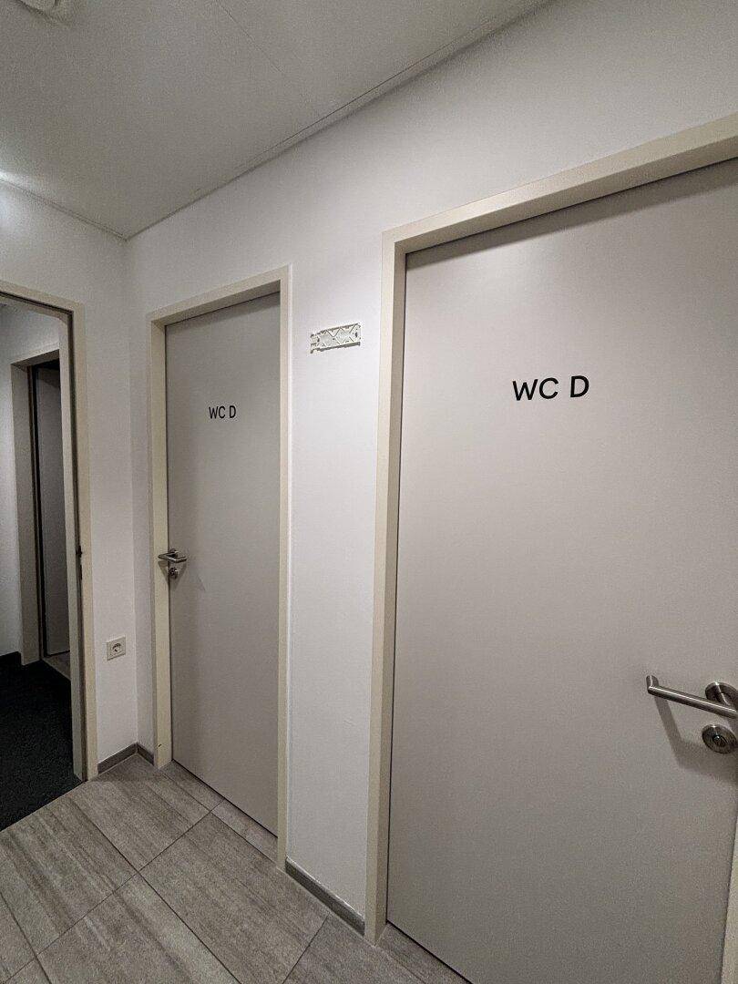 Flur in einem öffentlichen Waschraum mit zwei Türen, die zu den Toiletten führen.