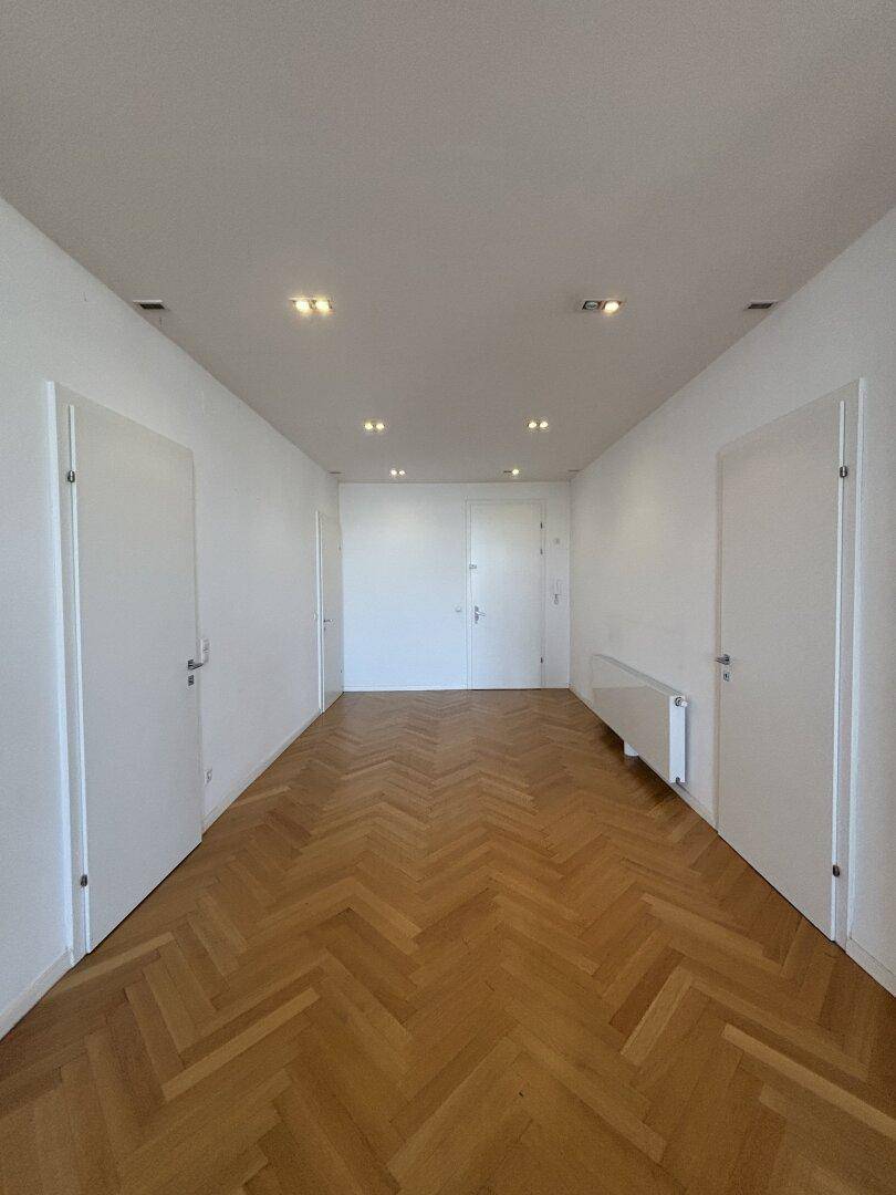Langer, heller Flur mit Fischgrätparkett und mehreren Türen.