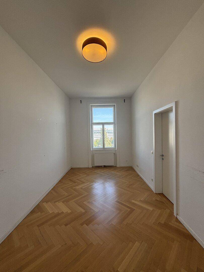 Helles, unmöbliertes Schlafzimmer mit Fischgrätparkett und Fenster.