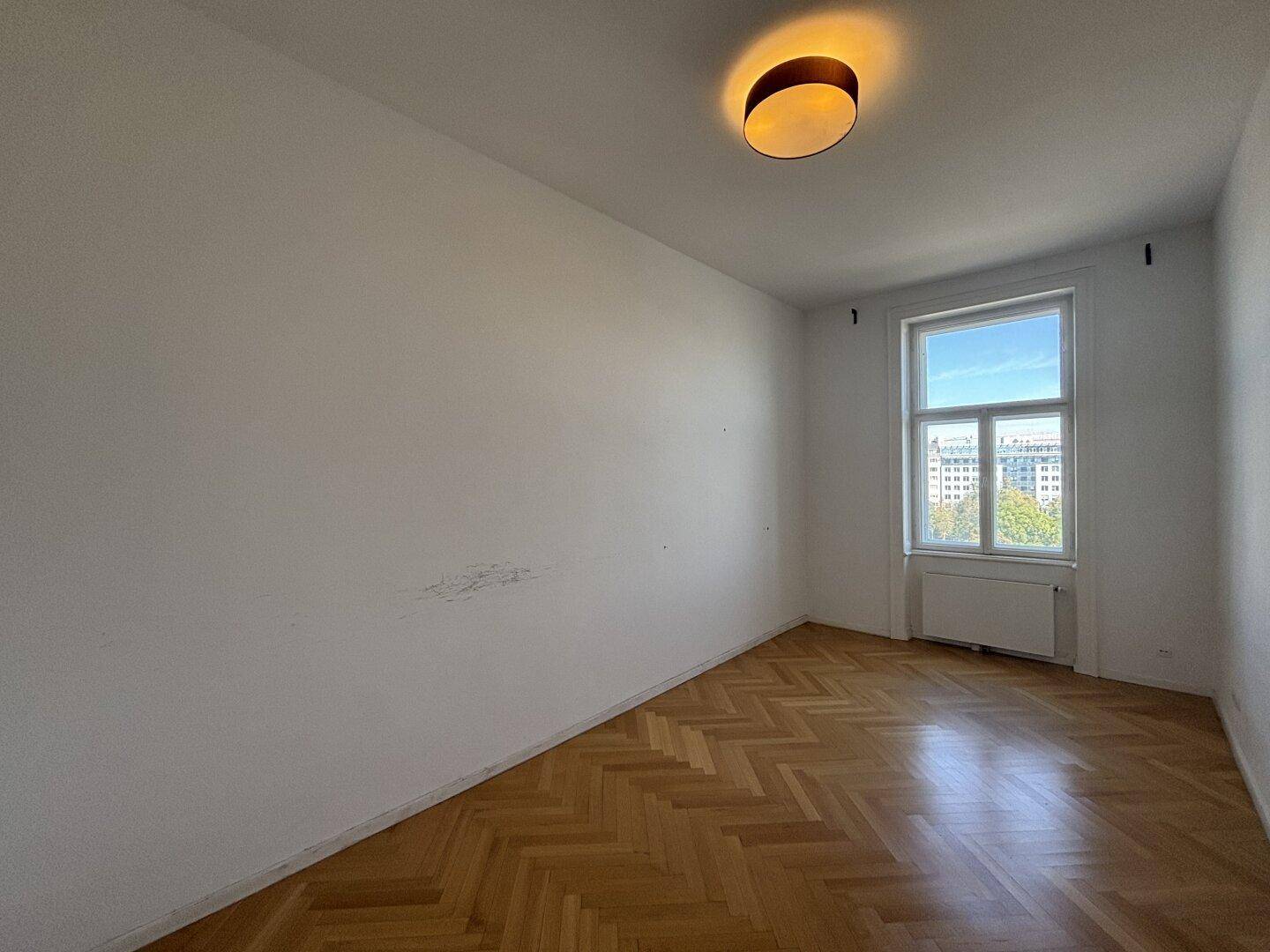 Helles, unmöbliertes Schlafzimmer mit Fischgrätparkett und Fenster.