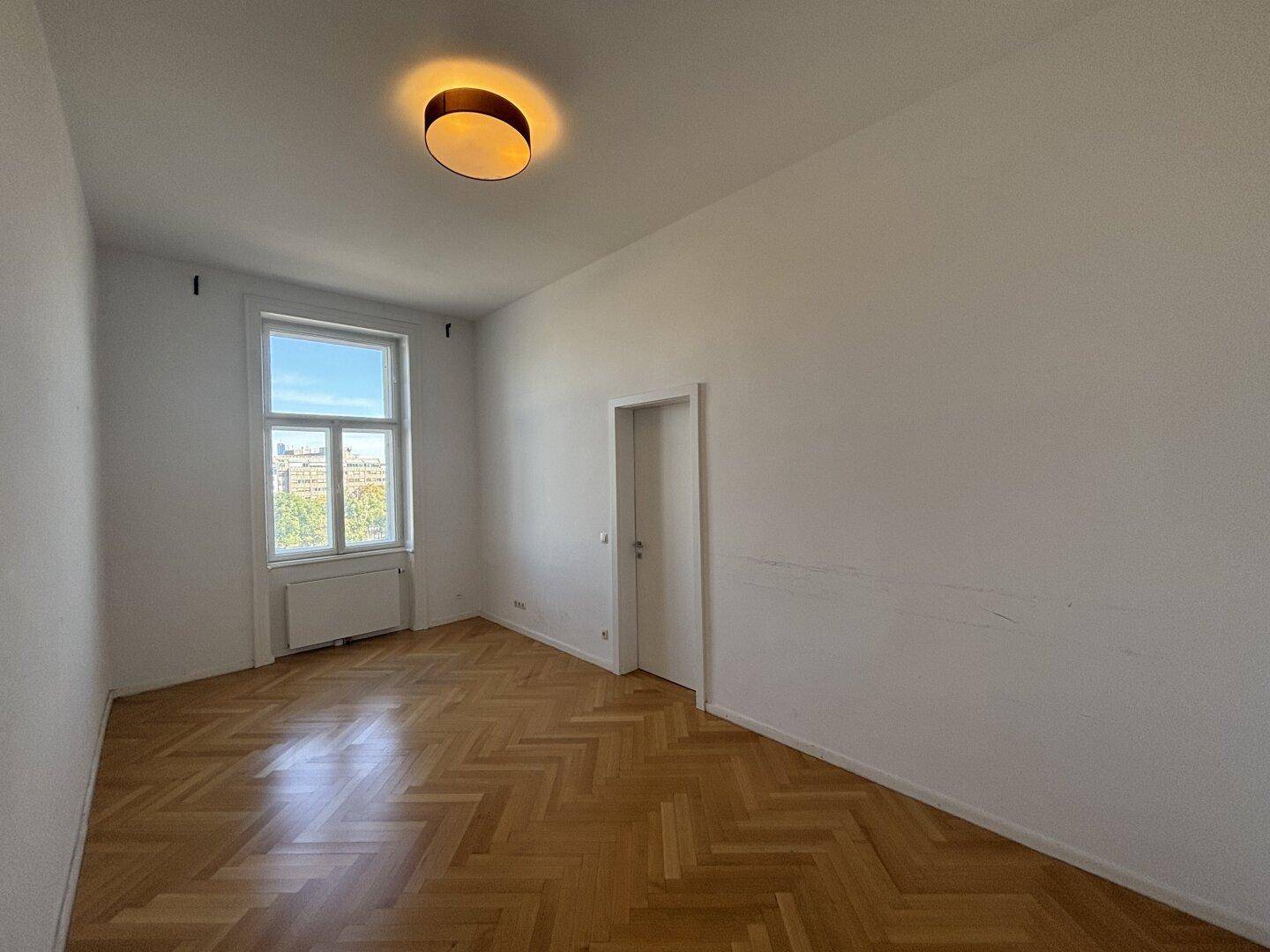Helles, unmöbliertes Schlafzimmer mit Fischgrätparkett und Fenster.