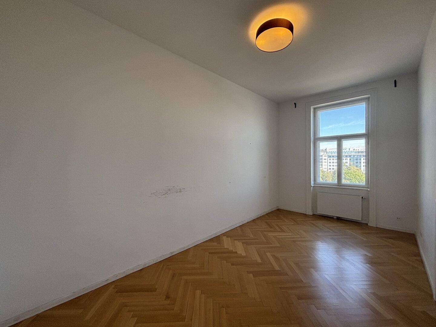 Helles, unmöbliertes Schlafzimmer mit Fischgrätparkett und Fenster.