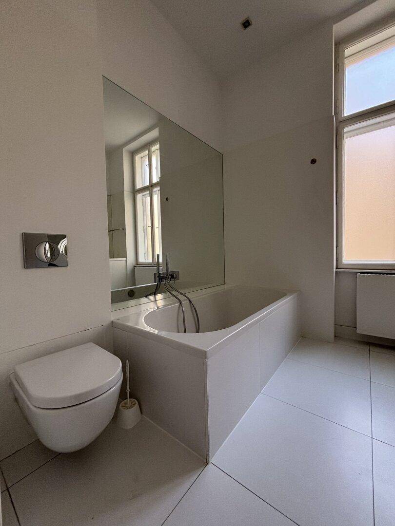 Helles Badezimmer mit Badewanne, Wand-WC und großem Fenster.