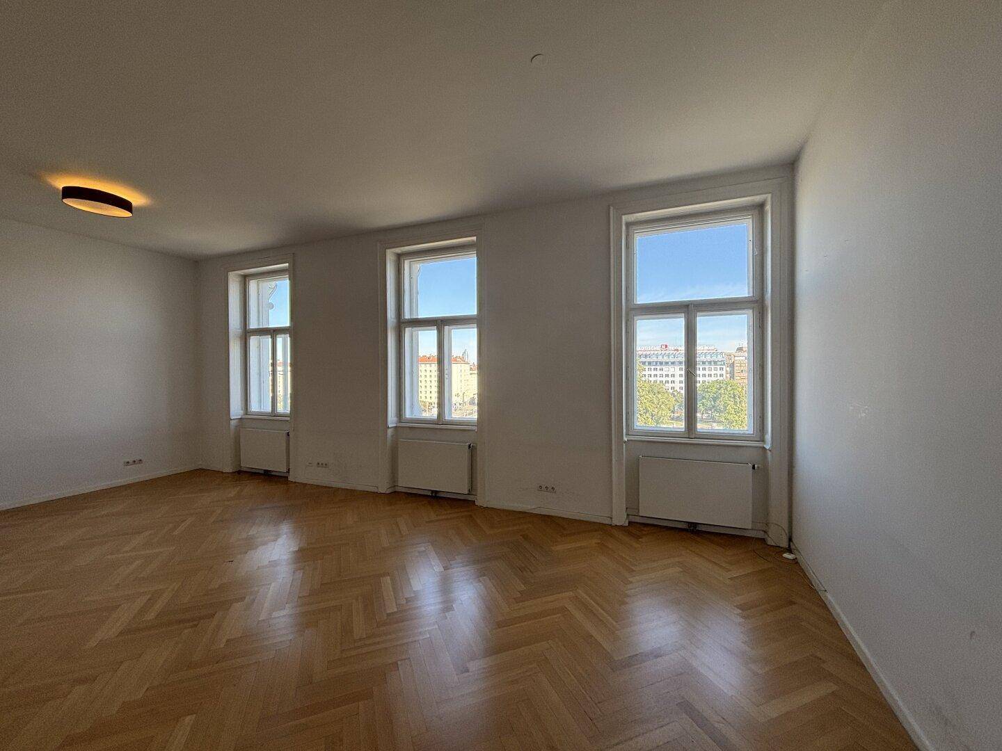 Geräumiges, unmöbliertes Wohnzimmer mit Fischgrätparkett und Stadtblick.