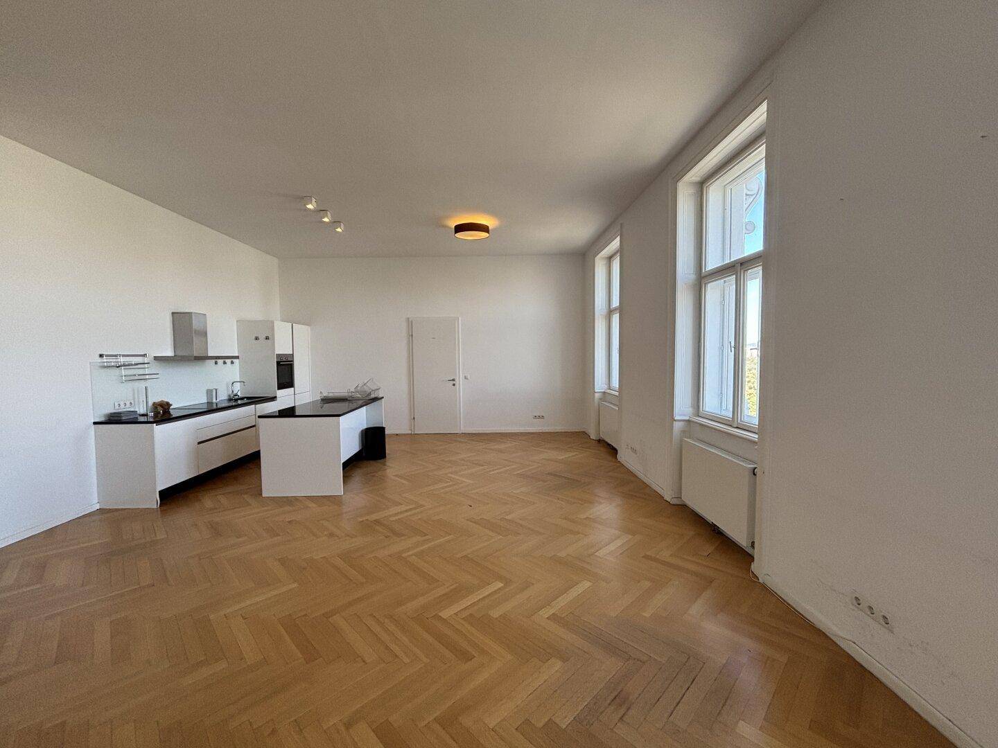 Geräumiger, unmöblierter Wohn- und Essbereich mit offener Küche und Fischgrätparkett.