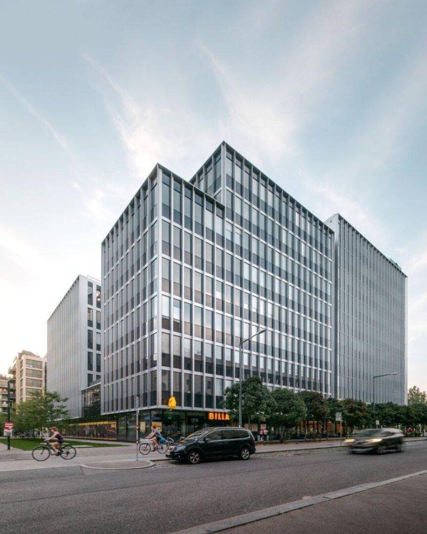 Modernes Geschäftsgebäude mit markanter Glasfassade und Einzelhandelsflächen im Erdgeschoss an einer belebten Stadtstraße.