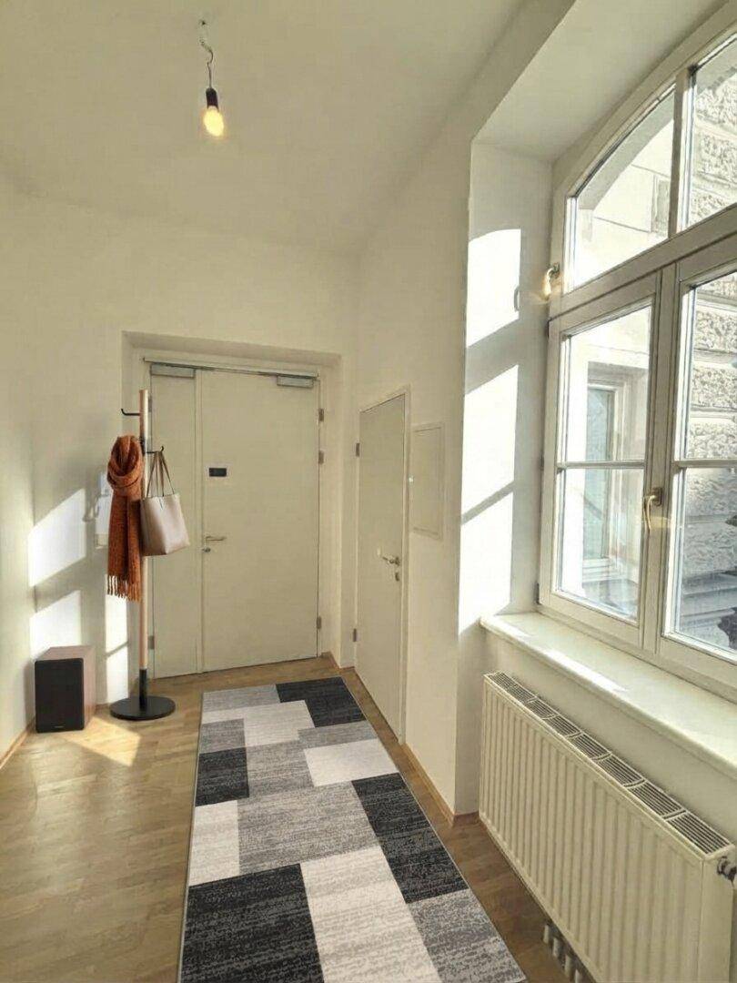 Heller Eingangsbereich mit Holzboden, großem Fenster und viel Tageslicht.