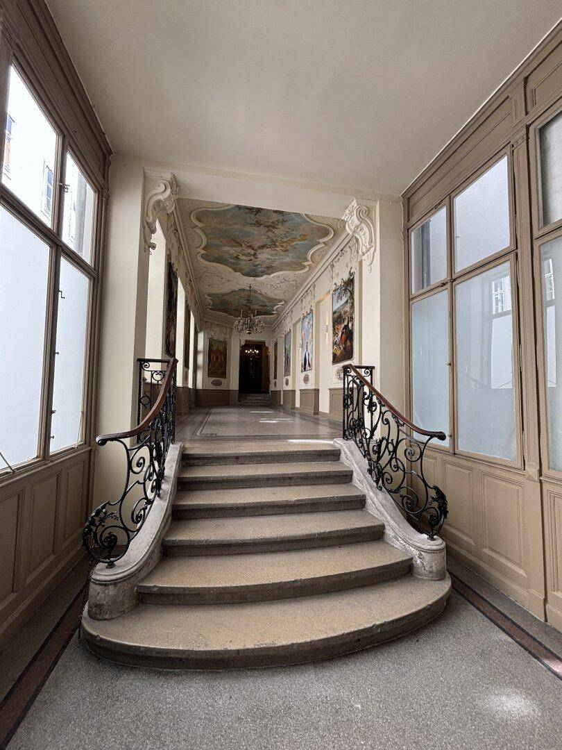 Prächtiges Treppenhaus mit kunstvollen Stuckdecken, Wandgemälden und schmiedeeisernem Geländer.