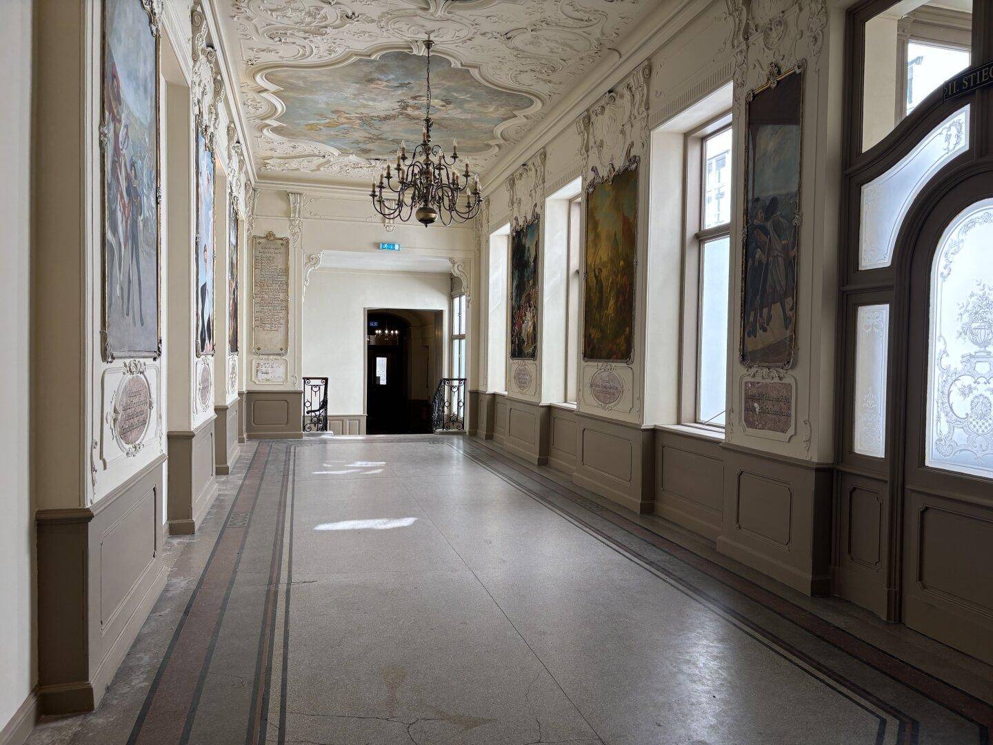 Historischer Flur mit aufwendigen Stuckdecken, Kronleuchter und großen Fenstern.
