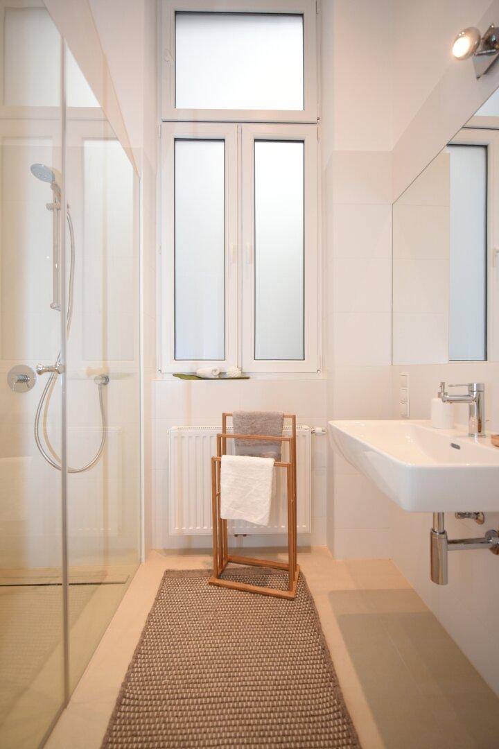 Helles Badezimmer mit Dusche, Einzelwaschbecken und Fenster.